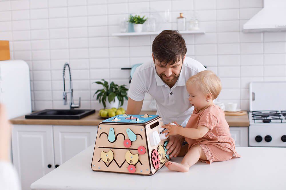 Baby spielt mit Busykids Tresor und Papa schaut zu